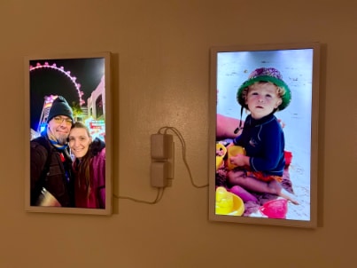 Two Electric Objects frames mounted side by side on a warm plaster wall, each showing a family photograph.